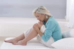 Mature person sitting on bed with arthritis pain in knee